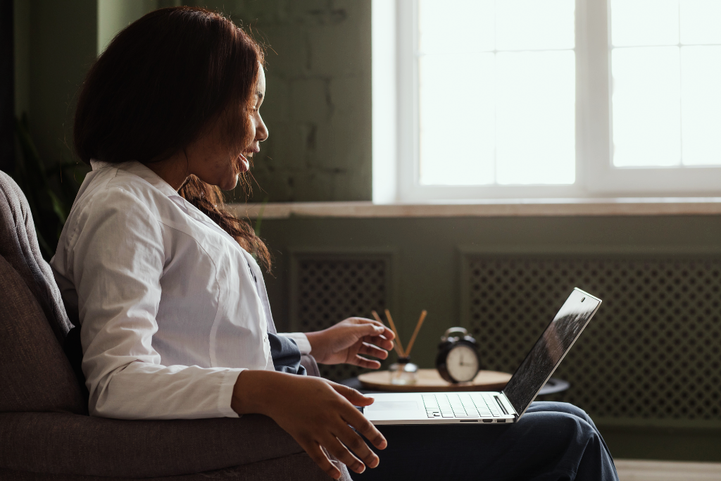 Choosing a therapist. A picture of a Black woman smiling and sitting on a couch with an open laptop on her lap.