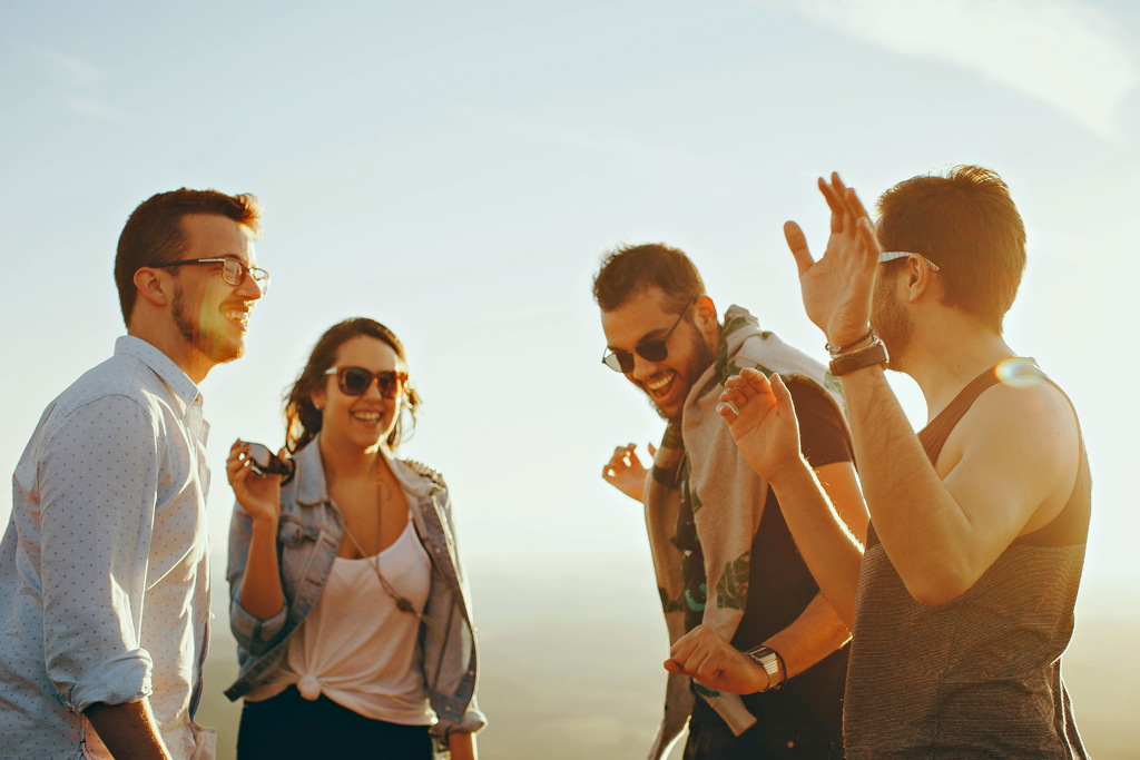 A photograph of four people standing outdoors, laughing.